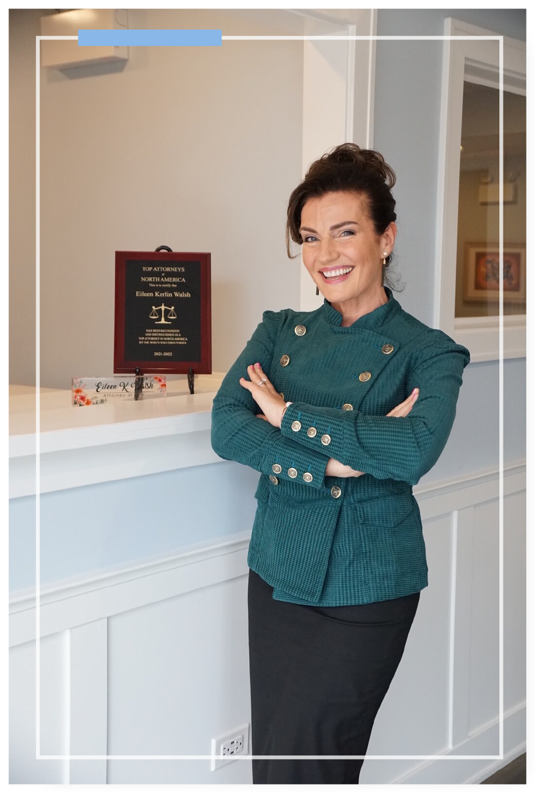 Eileen in her office standing next to her Top Attorneys of North America award