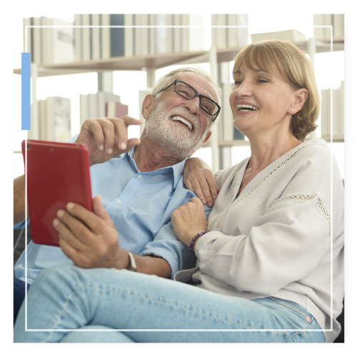 Mature couple sitting on a couch laughing at something they are looking at on a tablet