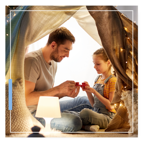 Father and daughter playing together under a tent made with blankets. class=
